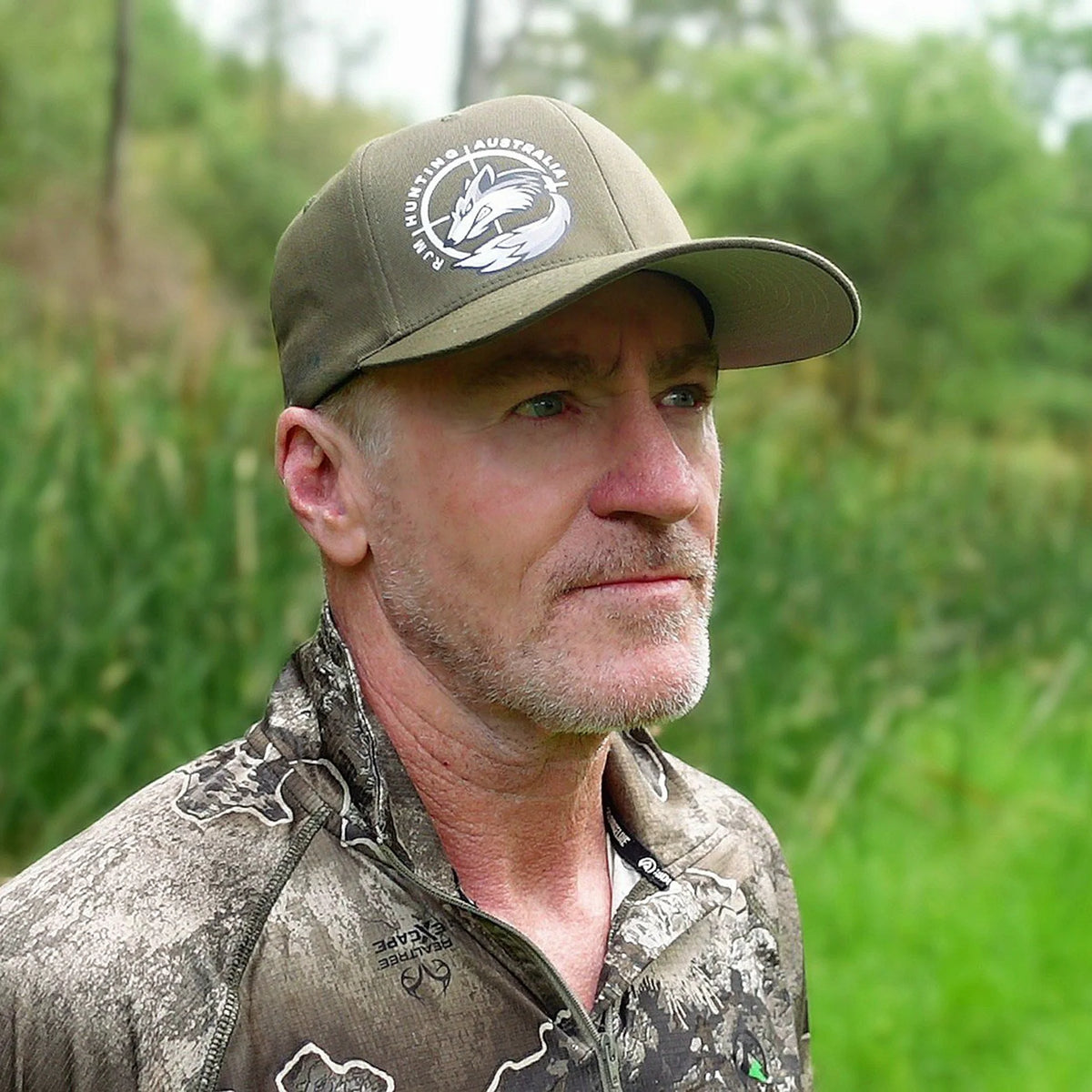 Man wearing an olive RJM Hunting Australia cap outdoors, side view with the fox logo