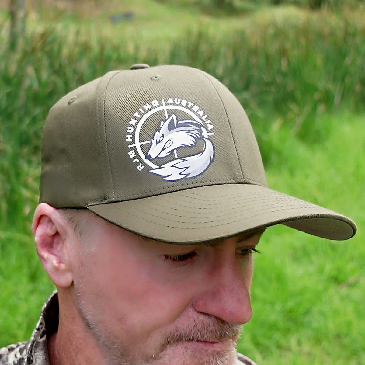 Close-up of an olive RJM Hunting Australia Flexfit cap with the white fox logo on the front